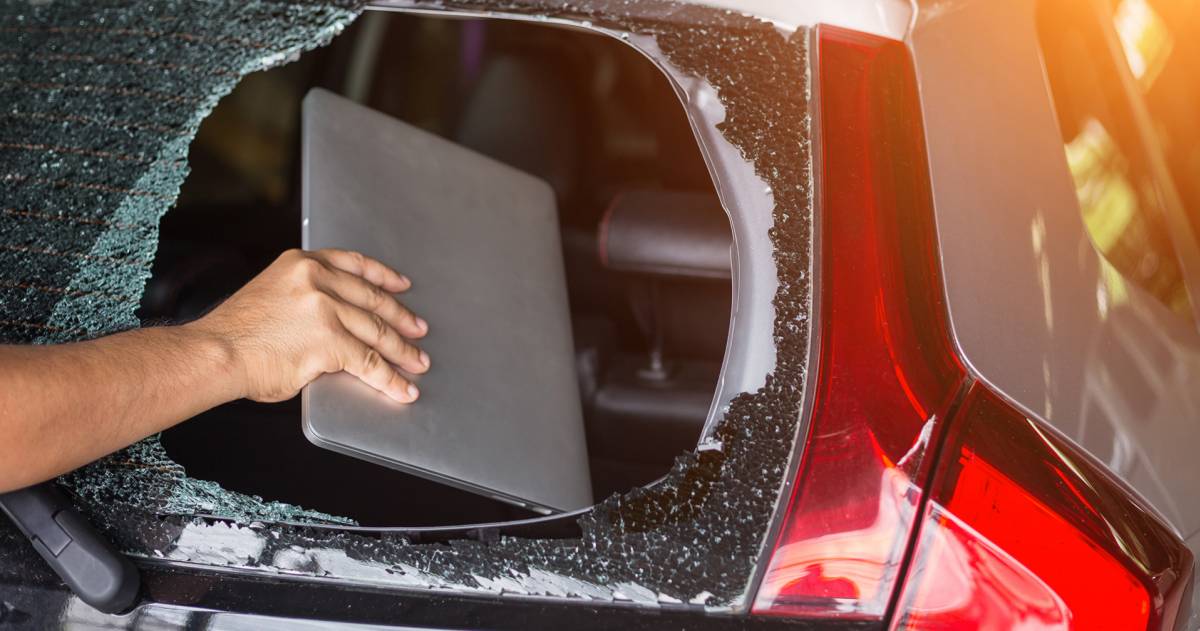 Auto inbraak; hand haalt via gebroken achterraam een laptop uit de auto